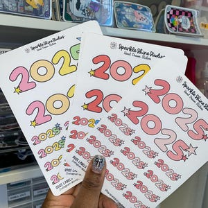 May include: Three sheets of stickers with various designs of the year 2025 in different colors. The stickers are on a white background and have a star design. The text "Sparkle Shine Studios" and "Hand Drawn Stickers" is on the top of the sheets.