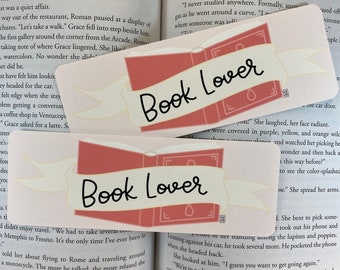 May include: Two pink and white bookmarks with the text "Book Lover" in black script. The bookmarks are layered with a book illustration and a ribbon.