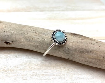 May include: A silver ring with a light blue gemstone set in a beaded bezel.