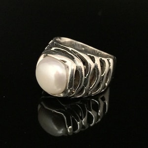 May include: A silver ring featuring a large white pearl set within a textured, cage-like design.