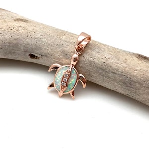 May include: A rose gold turtle pendant featuring a white opal stone and clear cubic zirconia accents.