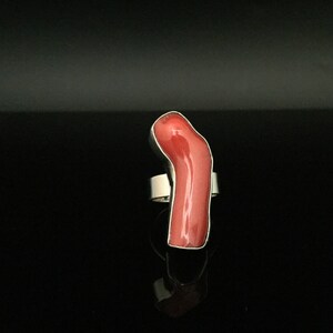 May include: A silver ring with a large, bright red coral stone. The stone is shaped like a long, thin, curved piece of coral.