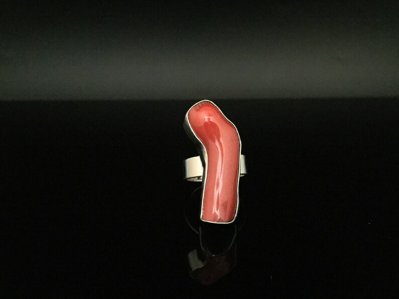 May include: A silver ring with a large, bright red coral stone. The stone is shaped like a long, thin, curved piece of coral.