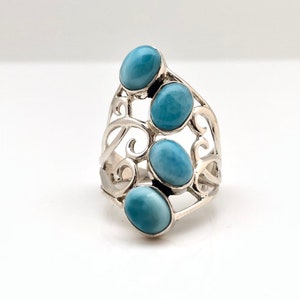 May include: A silver ring with a delicate, swirling design featuring four oval-shaped blue gemstones.