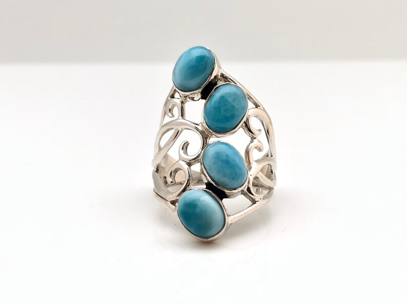 May include: A silver ring with a delicate, swirling design featuring four oval-shaped blue gemstones.