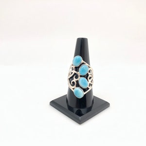 May include: A silver ring with a delicate, swirling design and five oval-shaped blue gemstones.