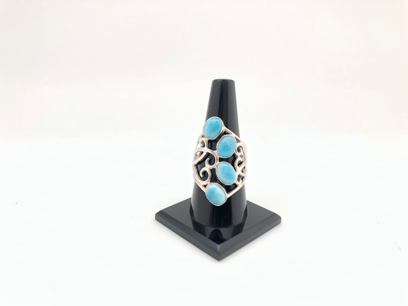 May include: A silver ring with a delicate, swirling design and five oval-shaped blue gemstones.