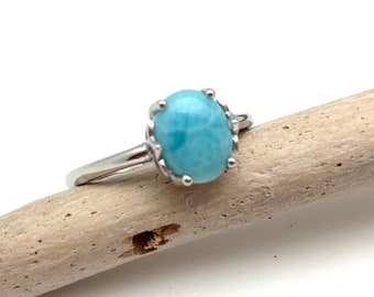 May include: A silver ring with a light blue oval-shaped gemstone. The gemstone has a swirling pattern.