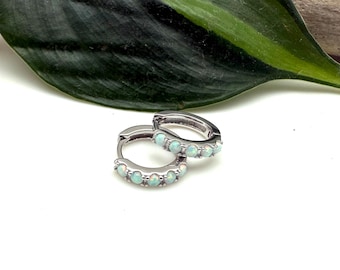 May include: A pair of silver hoop earrings with a row of small, light blue opal stones.