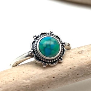 May include: A silver ring with a green and blue gemstone set in a decorative floral design.