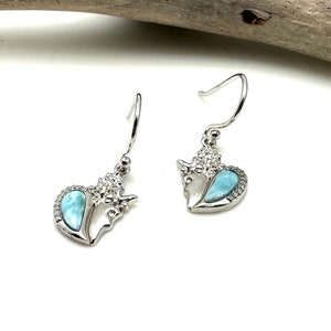 May include: A pair of silver dangle earrings with a heart-shaped blue opal gemstone and a silver floral design.