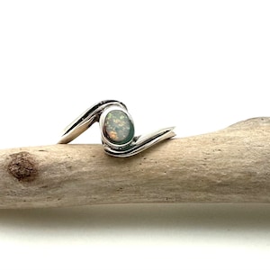 May include: A silver ring with a wavy band and a round opal gemstone.