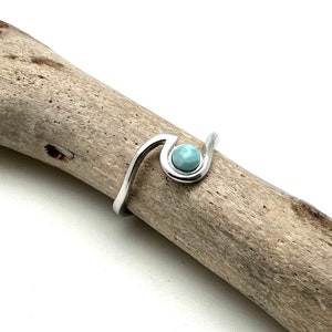 May include: A silver ring with a light blue gemstone set in a wave-like design.