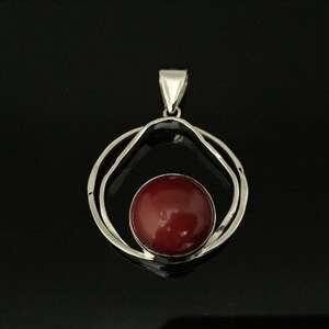 Pu&ograve; includere: Un ciondolo d'argento con una pietra preziosa rossa incastonata in un design a doppio cerchio.