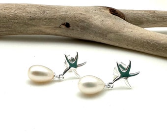 Puede incluir: Un par de pendientes de plata con una perla colgante y un diseño de estrella de mar.