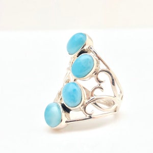 May include: A silver ring with a delicate, swirling design and four light blue oval-shaped gemstones.