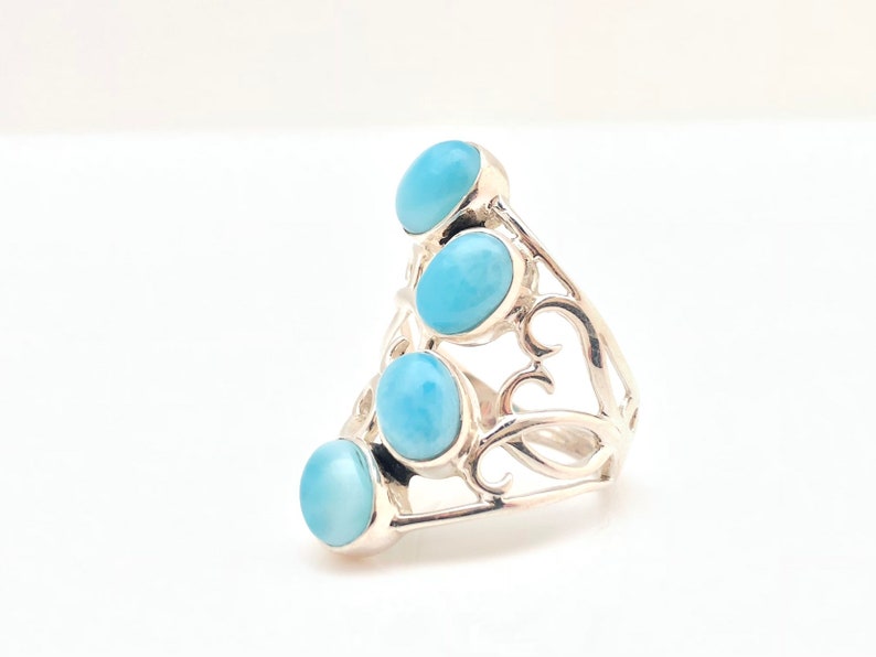 May include: A silver ring with a delicate, swirling design and four light blue oval-shaped gemstones.