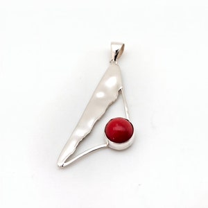 May include: A silver pendant with a red coral stone in the center. The pendant is shaped like a triangle with a curved edge.