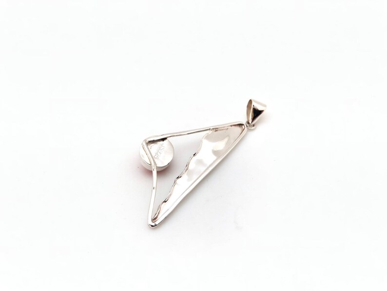 May include: Silver pendant with a triangular shape and a round, light pink stone set in the center. The pendant has a textured surface and a loop at the top for attaching a chain.