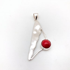 May include: A silver pendant with a red coral stone in the center. The pendant is shaped like a triangle with a curved, textured edge.