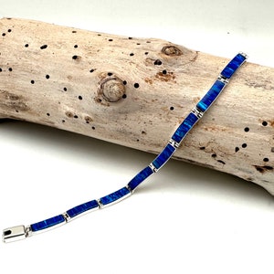 May include: A link bracelet featuring rectangular segments inlaid with vibrant blue iridescent stone. The bracelet is constructed with polished silver-toned metal frames connecting each individual blue stone piece, finished with a secure metal clasp.
