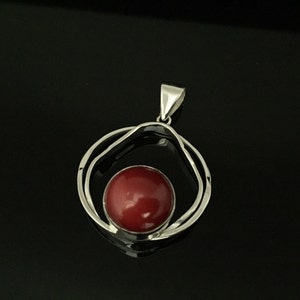Pu&ograve; includere: Un ciondolo d'argento con una pietra preziosa rossa incastonata in un design a doppio cerchio.