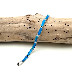 May include: A link bracelet featuring rectangular segments of vibrant blue opal inlay set within a polished silver-tone metal frame. The bracelet displays a repeating pattern of bright cyan and deep blue hues, secured by a metal clasp at the end.