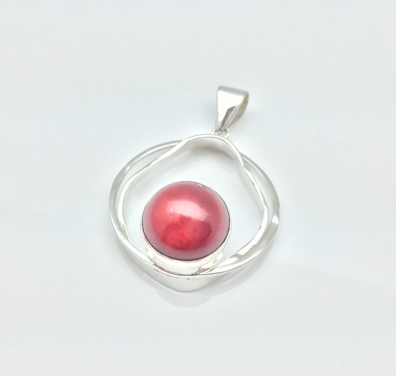 Pu&ograve; includere: Un ciondolo d'argento con una pietra preziosa rossa incastonata in un design a doppio cerchio.