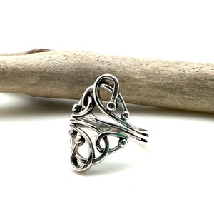 May include: A silver ring with a unique, intricate design featuring multiple loops and small beads. The ring is made of a single piece of metal and has a smooth, polished finish.