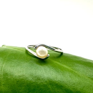 May include: A silver ring with a single white pearl set in a curved band.