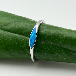 May include: A silver ring with a blue opal gemstone set in a curved band.