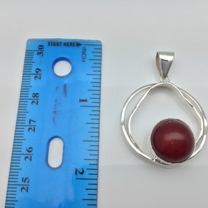 Pu&ograve; includere: Ciondolo in argento con una pietra preziosa rossa incastonata in un design a doppio cerchio. Il ciondolo misura circa 2,5 cm di diametro.