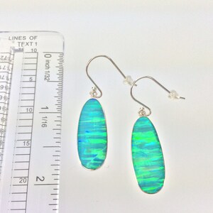 Peut inclure: Une paire de boucles d'oreilles pendantes en argent avec des pierres d'opale ovales vertes et bleues. Les boucles d'oreilles mesurent environ 2,7 cm de long.