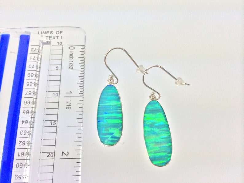 Peut inclure: Une paire de boucles d'oreilles pendantes en argent avec des pierres d'opale ovales vertes et bleues. Les boucles d'oreilles mesurent environ 2,7 cm de long.