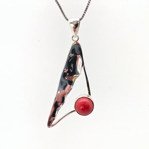 May include: A silver pendant necklace with a textured, abstract silver design and a red coral stone.