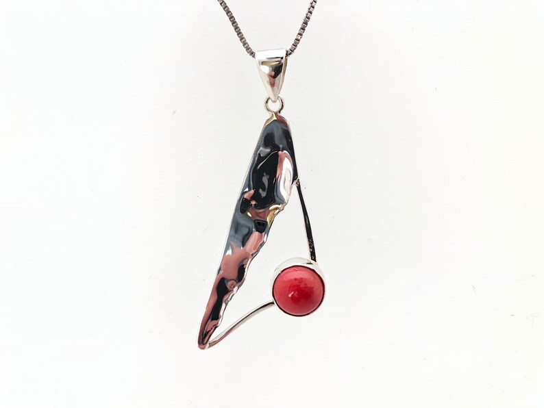 May include: A silver pendant necklace with a textured, abstract silver design and a red coral stone.