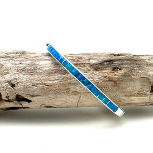May include: A silver bangle bracelet with a row of blue opal stones.