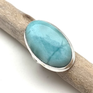 May include: A silver ring with a large oval-shaped blue gemstone. The gemstone has a marbled pattern and a light blue color.