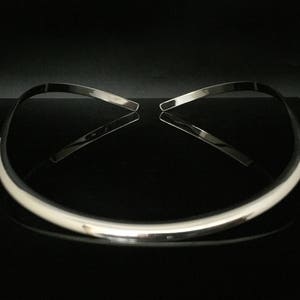May include: A silver choker necklace with a smooth, rounded surface. The necklace is displayed on a black background.
