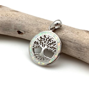 May include: A silver tree of life pendant with a white opal inlay. The pendant is round and has a delicate design.