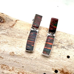Puede incluir: Un par de pendientes colgantes de plata con detalles de piedra iridiscente roja, verde y negra.