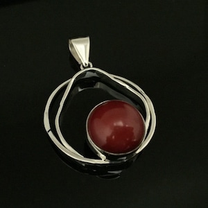 Pu&ograve; includere: Un ciondolo d'argento con una pietra preziosa rossa incastonata in un design a doppio cerchio.