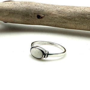 Può includere: Un anello d'argento con una pietra ovale bianca incastonata al centro. L'anello è semplice ed elegante.