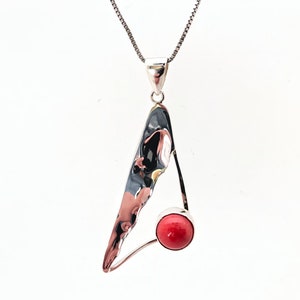 May include: A silver pendant necklace with a red coral stone. The pendant is shaped like a triangle with an abstract design.