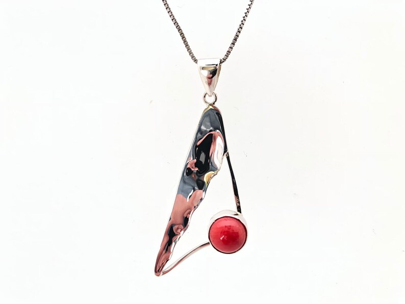 May include: A silver pendant necklace with a red coral stone. The pendant is shaped like a triangle with an abstract design.