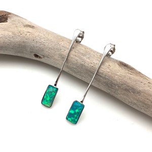 Puede incluir: Un par de pendientes de plata con piedras de ópalo verde. Los pendientes son largos y delgados, con un diseño sencillo.