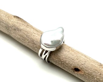 May include: A silver ring with a large, white, irregular shaped pearl set in the center. The ring has a twisted band.