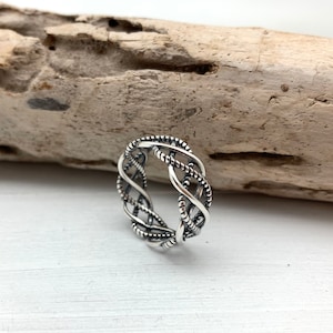 May include: A silver ring with a braided design. The ring is made of multiple strands of silver wire that are twisted together to create a complex pattern.