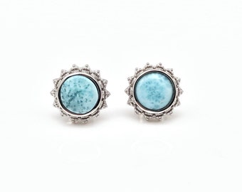 May include: A pair of silver earrings with a blue gemstone in the centre of each earring. The gemstones are surrounded by a silver filigree design.