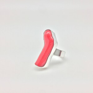 May include: A silver ring with a bright red, abstract, resin-like stone.
